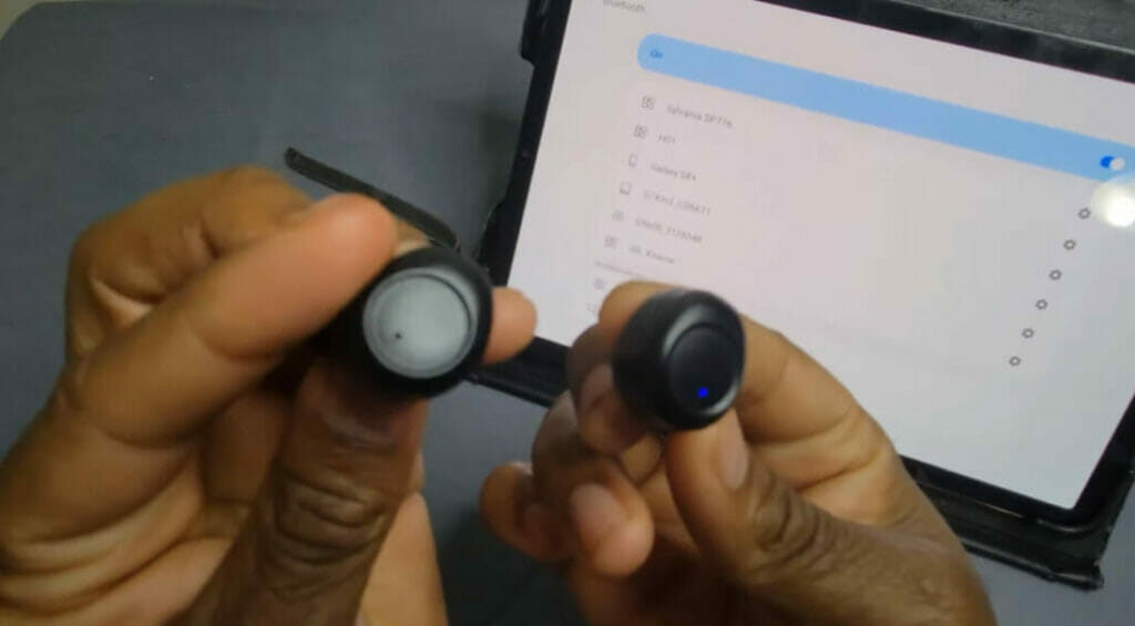 hand holding a pair of wireless earbuds trying to pair it on an iPAD