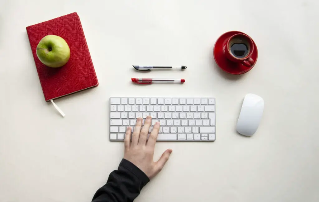 45619706 man hands on wireless keyboard with red notebook green apple and red cup of coffee on white table