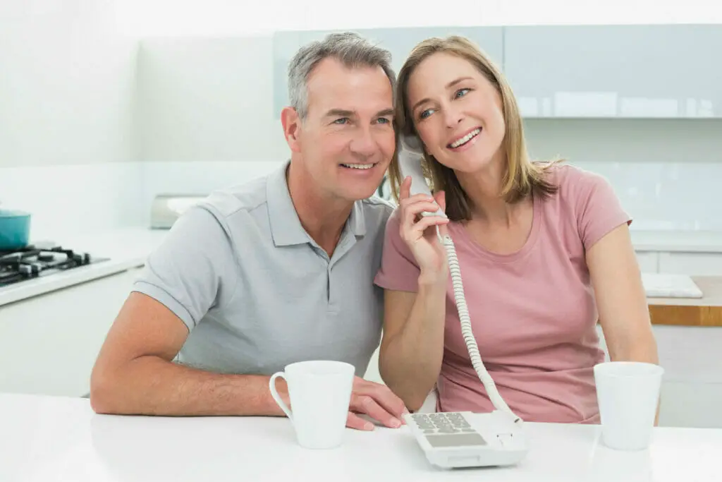 a happy couple sitting at their kitchen table with coffee using a landline phone