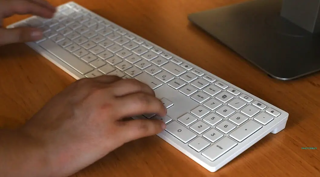 man typing on his wireless white keyboard