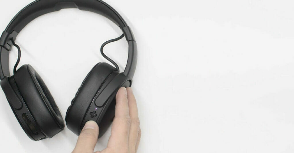top shot of a hand holding a black wireless headphone in a white background