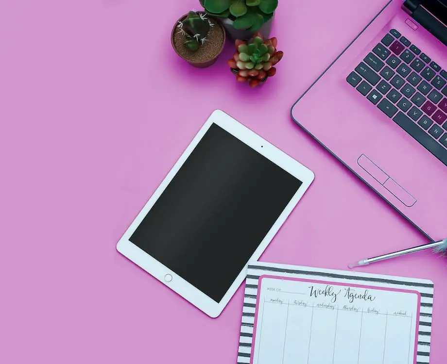 ipad, laptop and a weekly calendar on a pink background