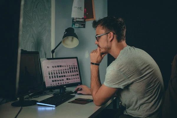 man working on her dual monitor computer station