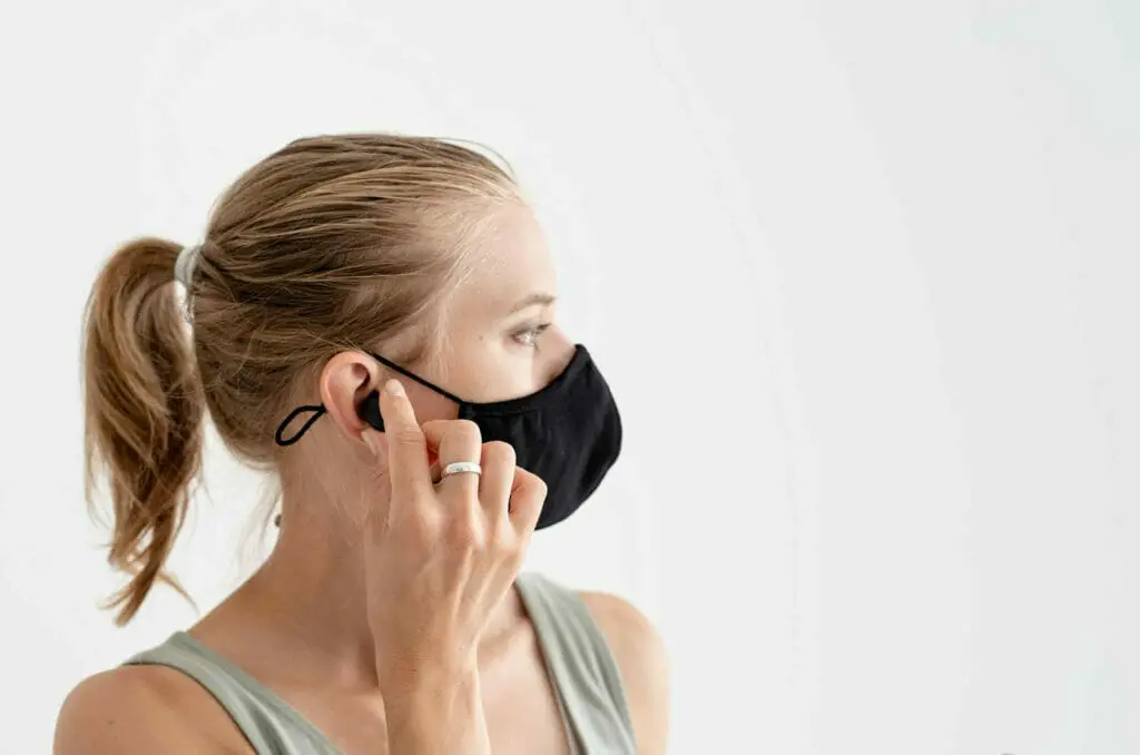 woman in a black facemask putting her earbud