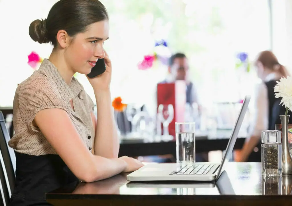 woman on a resto-cafe working on her laptop while calling someone on her phone