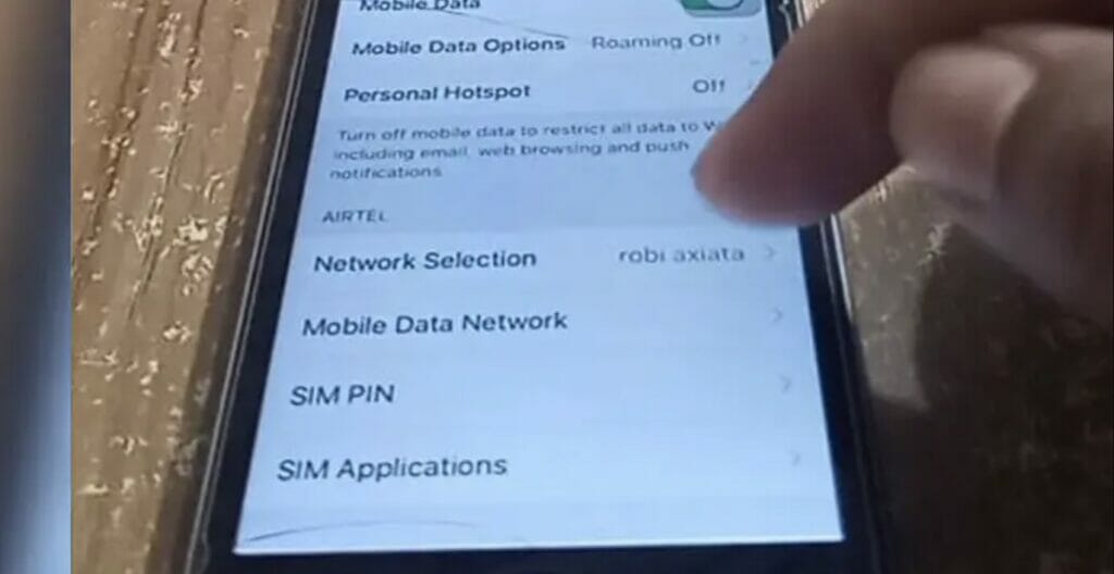 A person tapping Mobile Data Network setting on the phone that's on a table