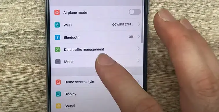 a hand tapping the More option on the phone setting menus