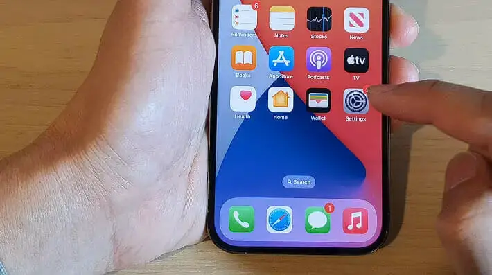 a man's left hand holding up an iphone while the right hand's pointer finger is tapping the Setting icon