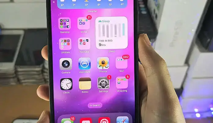 A person is holding up an iphone in a store showing its homescreen
