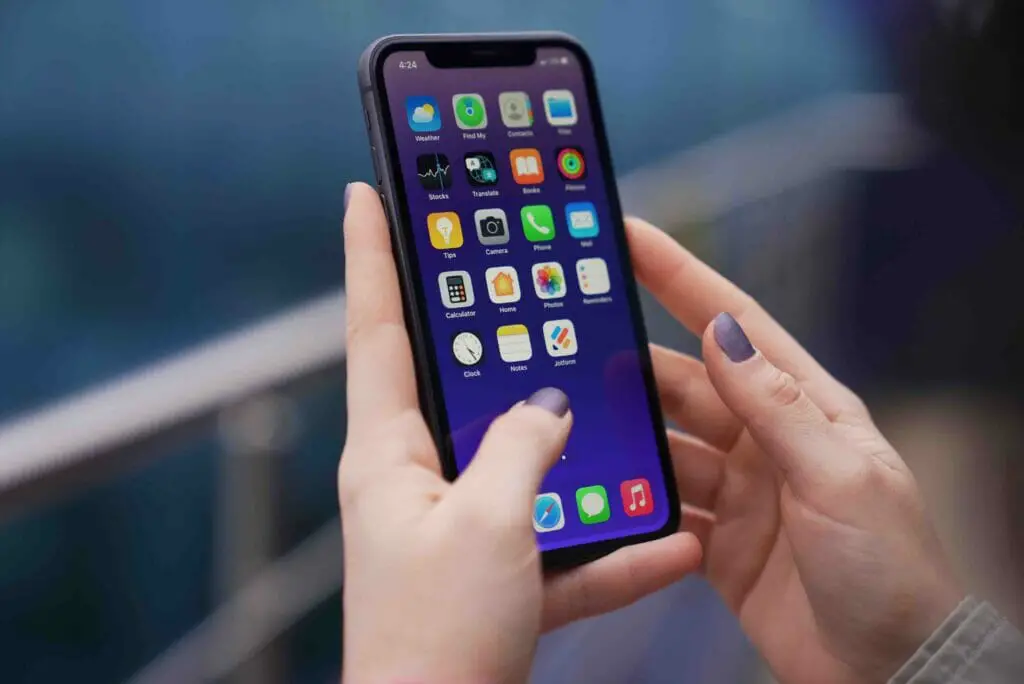 A woman's hand holding up her phone showing the homescreen icons