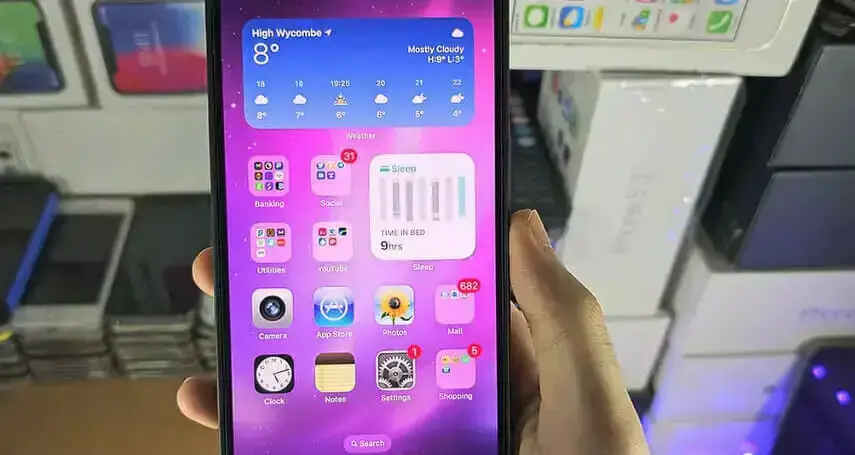 a person's left hand holding a phone showing the homescreen with app icons