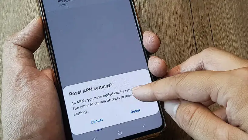 A hand holding a phone and tapping on the Reset APN option
