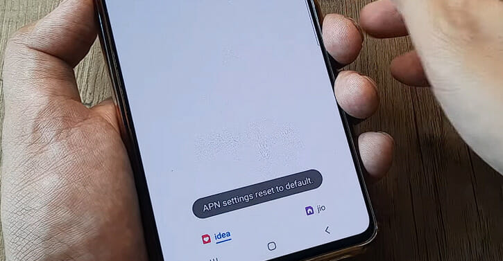 A person holding the phone and looking at the APN setting reset option