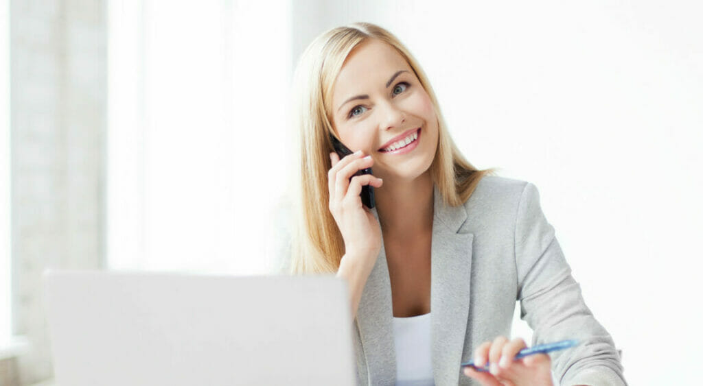 A business woman smiling and talking on the phone while sitting in front of a laptop