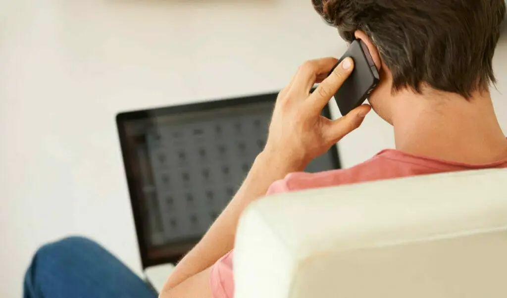 A man sitting on a couch with a laptop and a cell phone on his ear