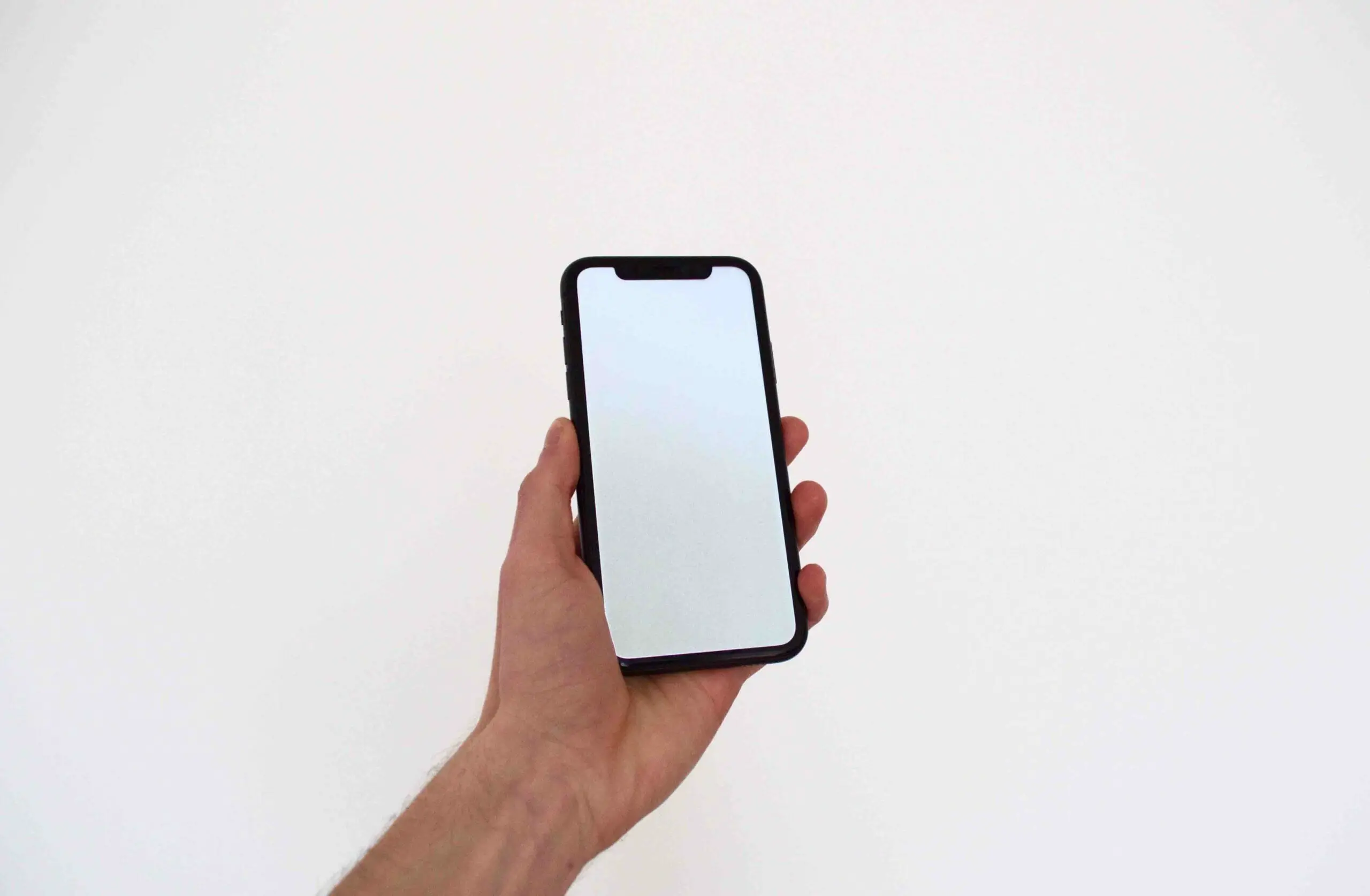 A man's left hand holding up a phone with just plane white background