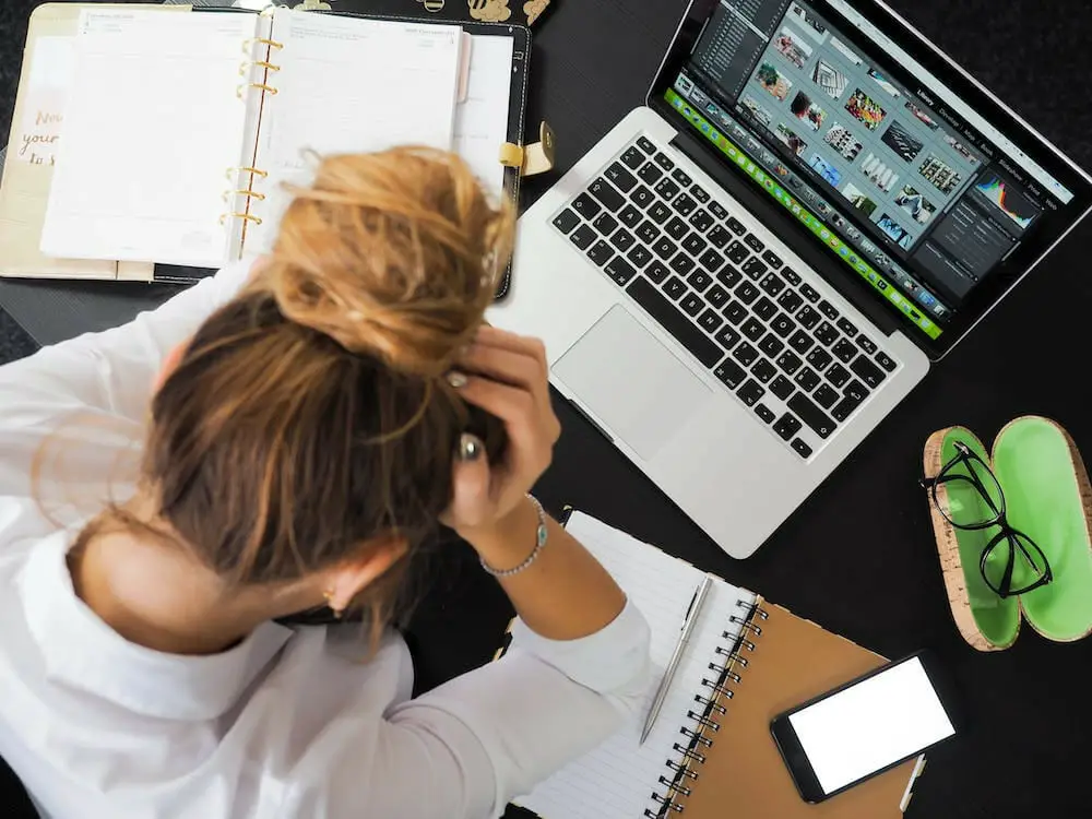 A woman holding up her head is sitting at a desk with a laptop