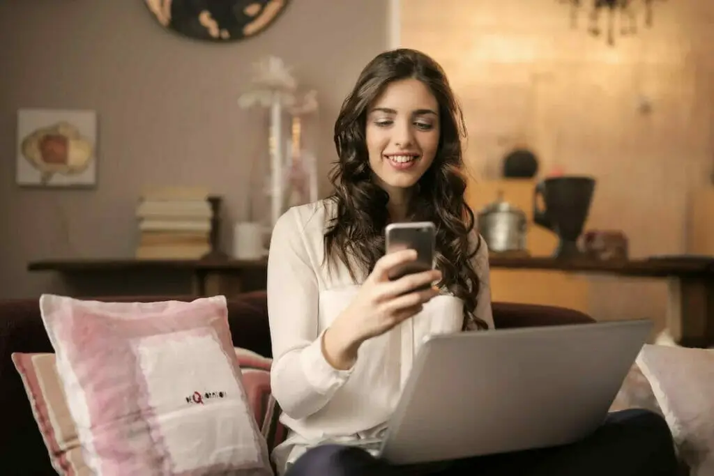 A woman sitting on a couch using her phone and laptop