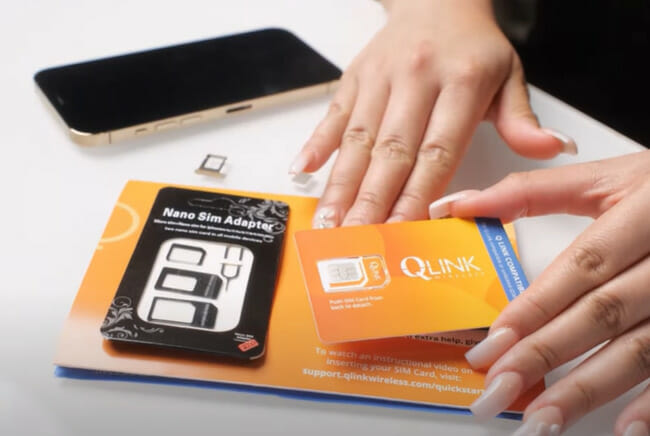 A woman's hand is holding a phone a Qlink sim card