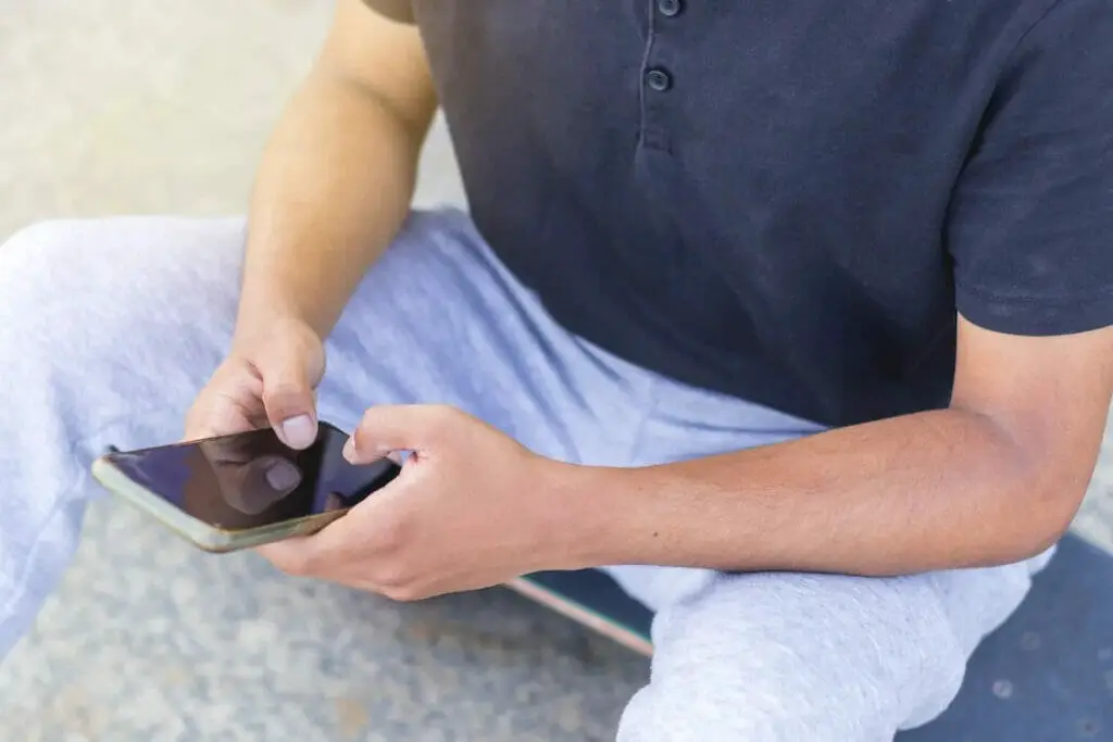 A man is sitting on a skateboard and using a cell phone