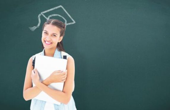 A young woman holding a laptop in front of a chalkboard