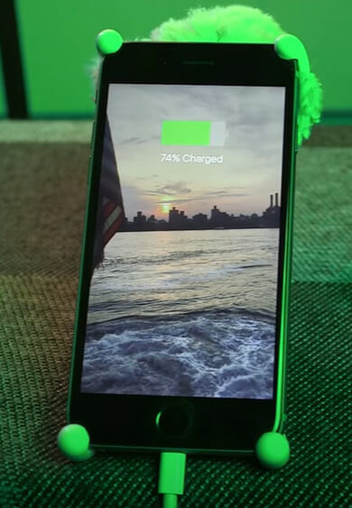 A green phone at 74% charged sitting on a green phone stand