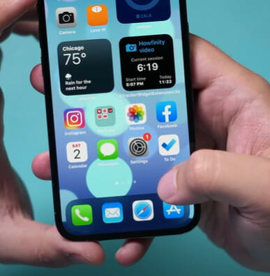 A person is holding up an iphone with a lot of apps on it