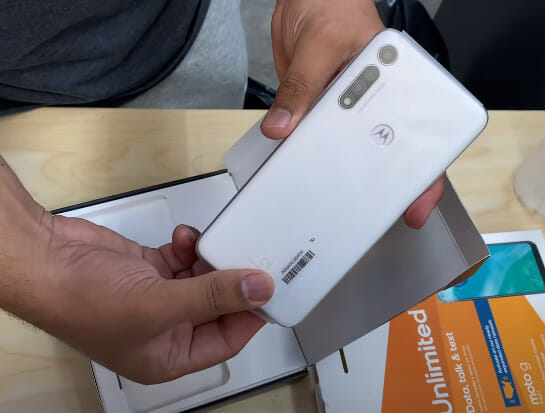 A person holding a white motorola phone in a box