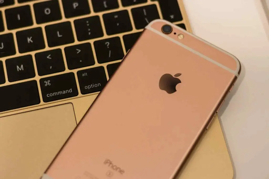 An iphone 6s is sitting next to a gold keyboard.