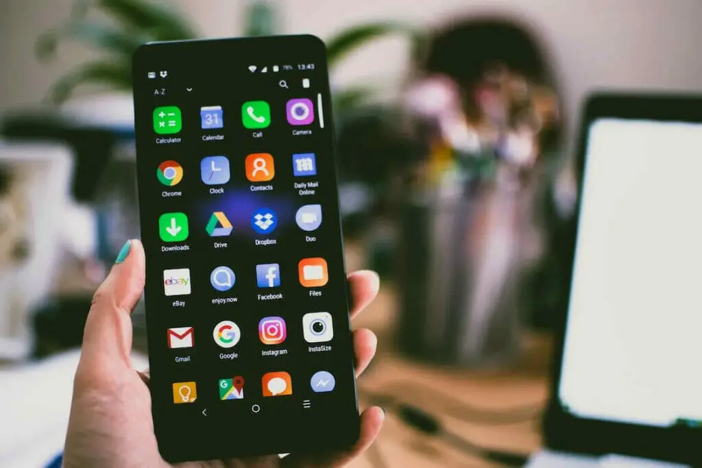 A person holding up a black smartphone with a lot of icons on it.