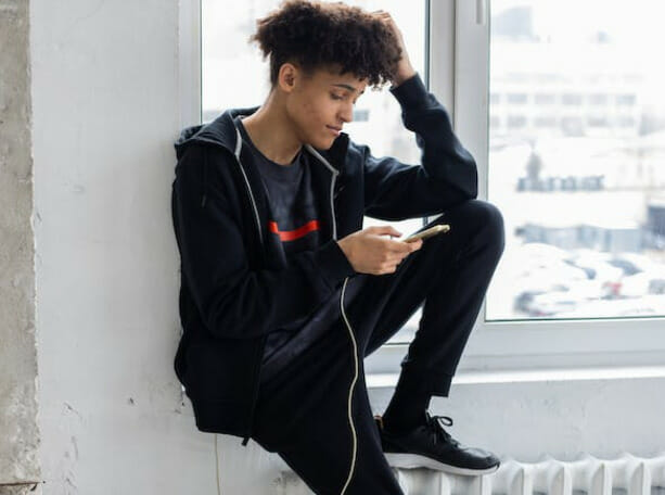 A young man sitting on a window sill looking at his phone
