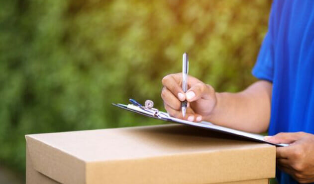 A delivery man is writing on a clipboard in front of a box