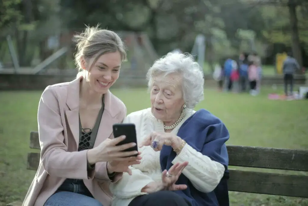 A woman and a senior citizen woman sitting at the park while looking at a phone