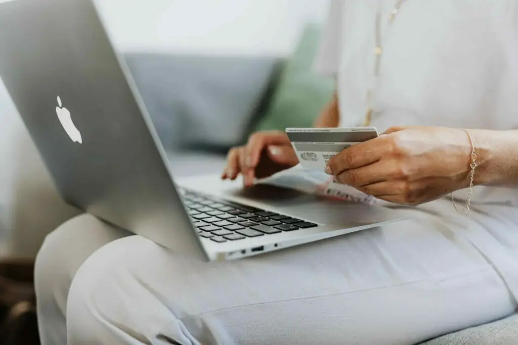 A woman sitting in a couch with laptop on her lap entering her credit card information