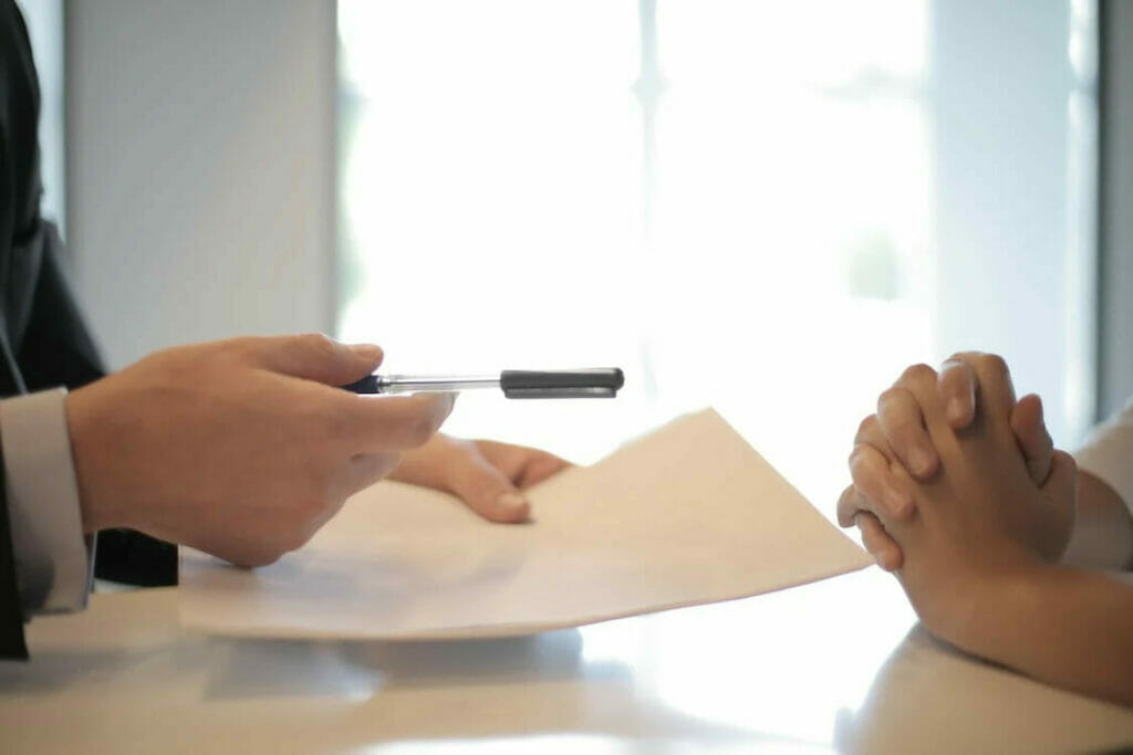 Two people talking on a table while the other person is holding a pen and paper