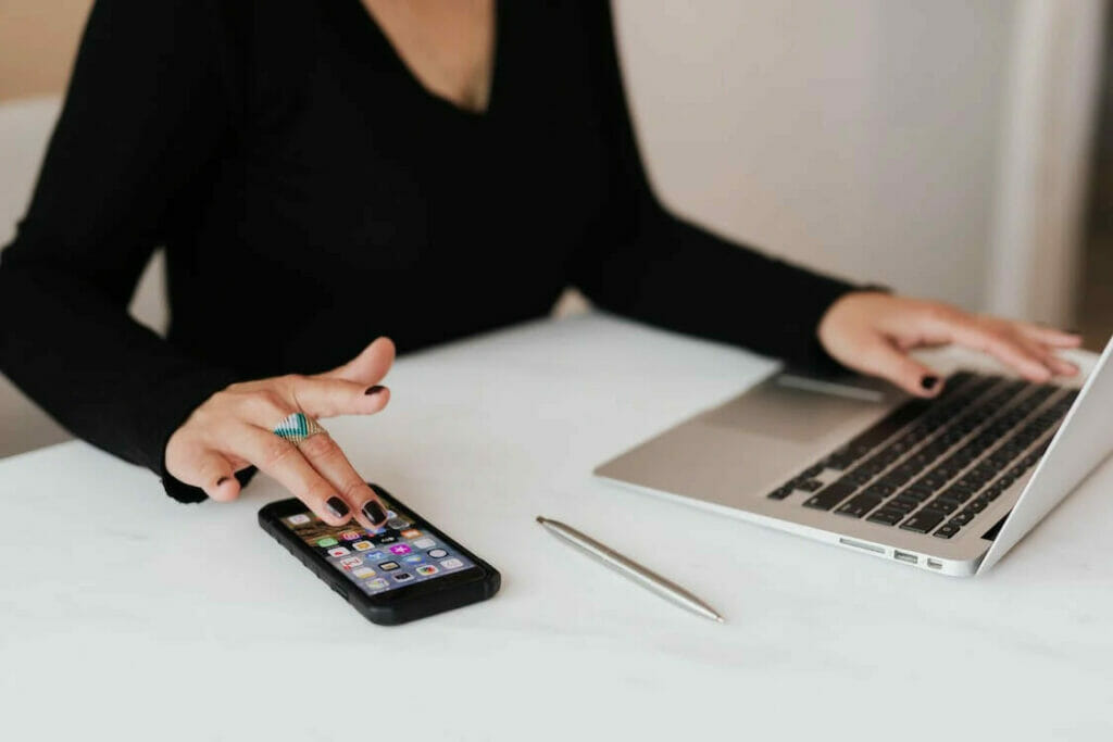 A woman using her phone and laptop on a white table