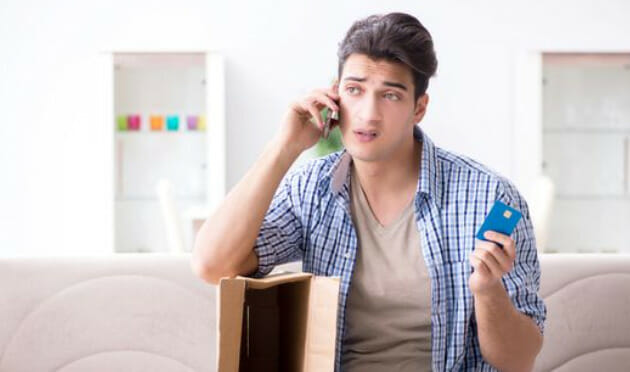 A man sitting on a couch holding a credit card and talking on the phone