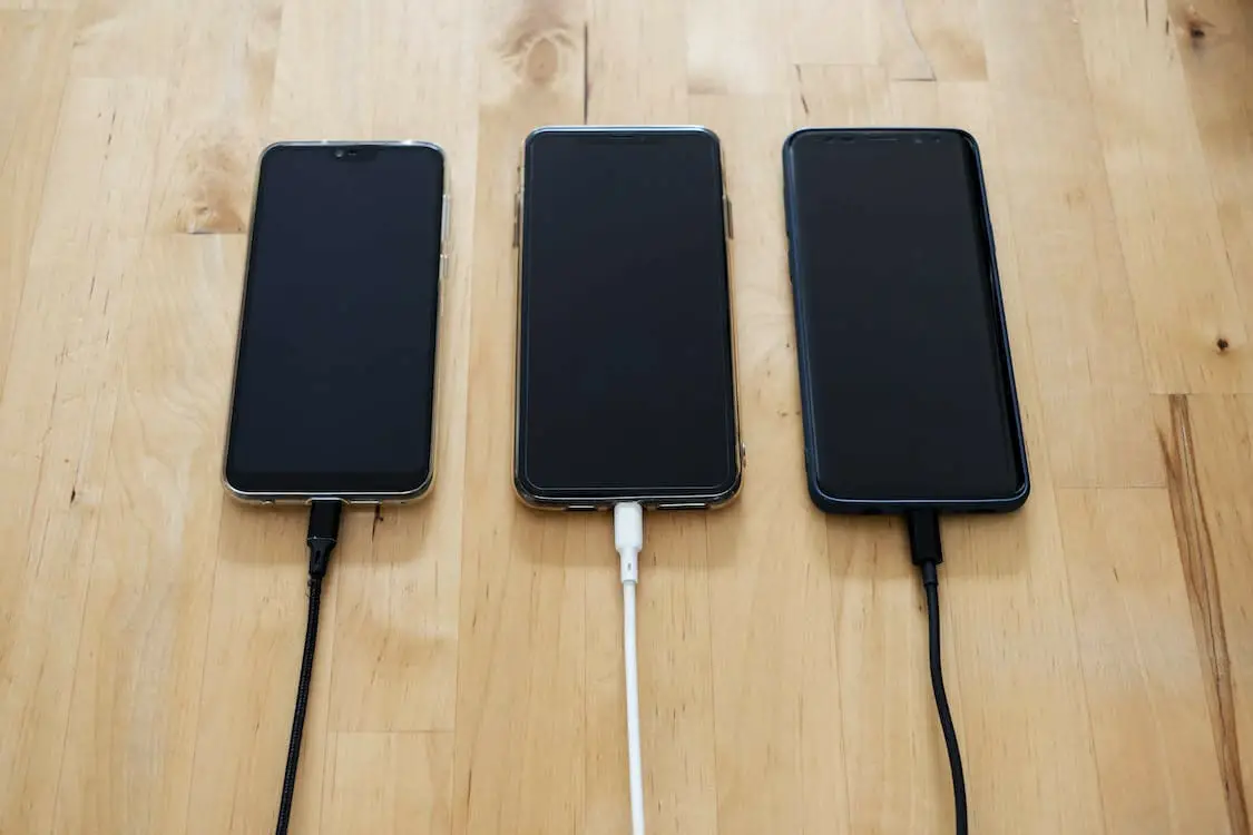 Three smartphones are connected to a charger on a wooden table