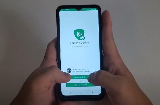A hand is holding up a phone with a screen showing the Find My Device app