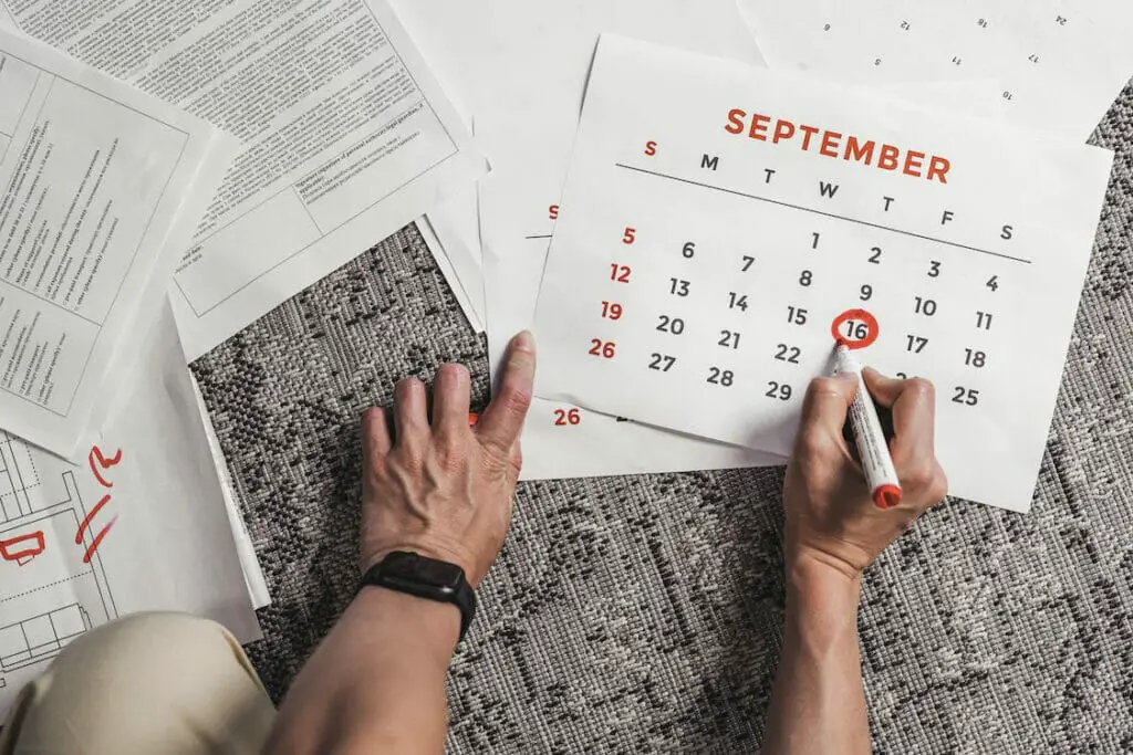 A person marking the 16th of September on a calendar paper placed on a carpeted floor