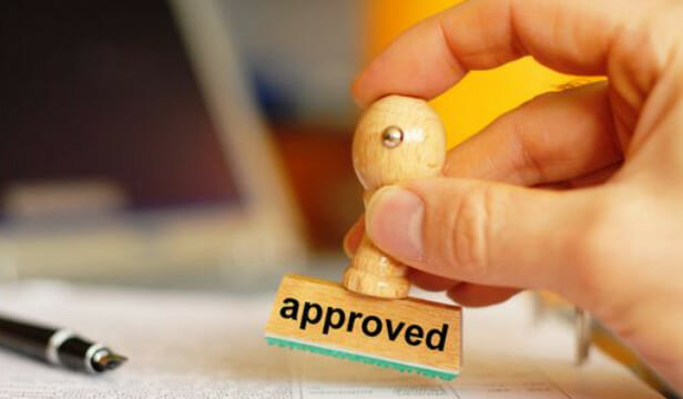 A person holding a wood paper stamp with the word approved in it