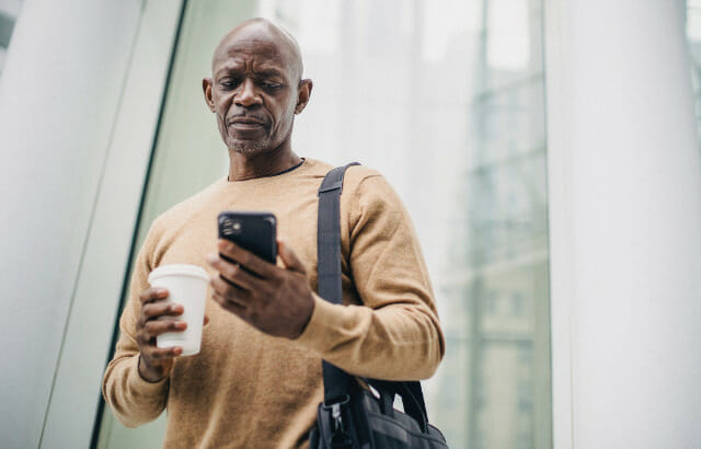 A man standing with cup on his right hand and a mobile phone on his left hand