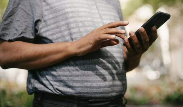 A man in gray stripe is holding and using his phone