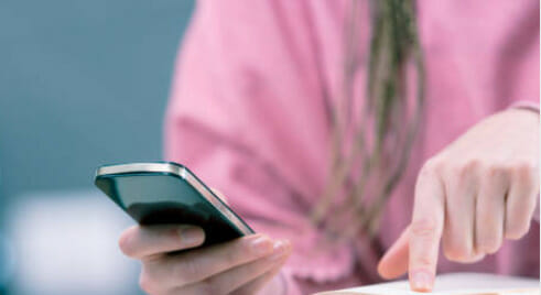 A woman is using a cell phone while reading a book