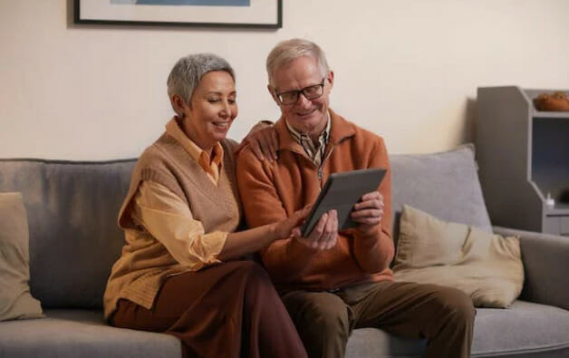 An older couple sitting on a couch and using a tablet computer