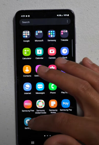 A person's hand tapping on the Setting icon of a phone that is on a table