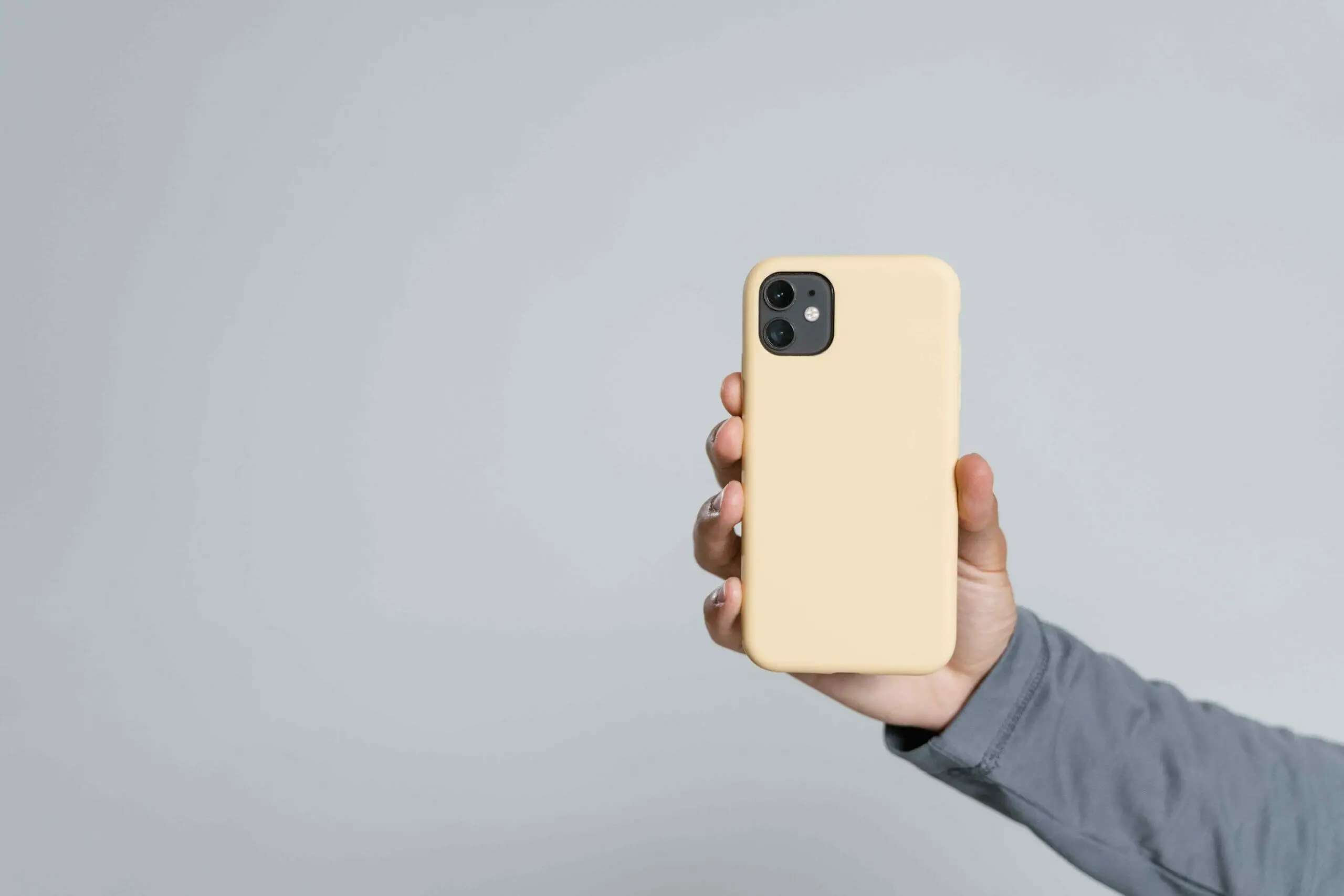 A hand holding and showing up a phone with yellow nude case color in a gray background