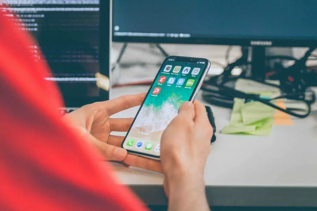 A man in a red shirt sitting on his working desk holding his phone