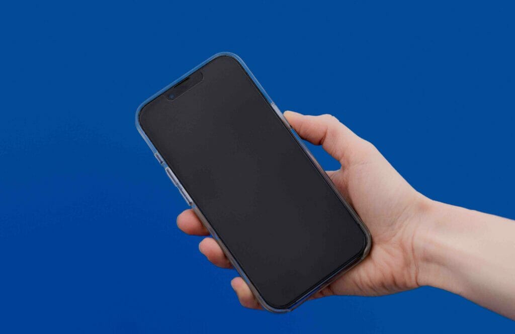 A hand holding a black iphone on a blue background.