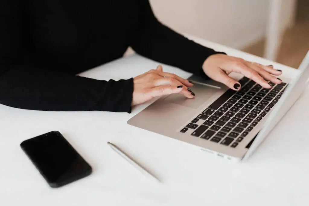 A woman working on her laptop with pen and cellphone besides it